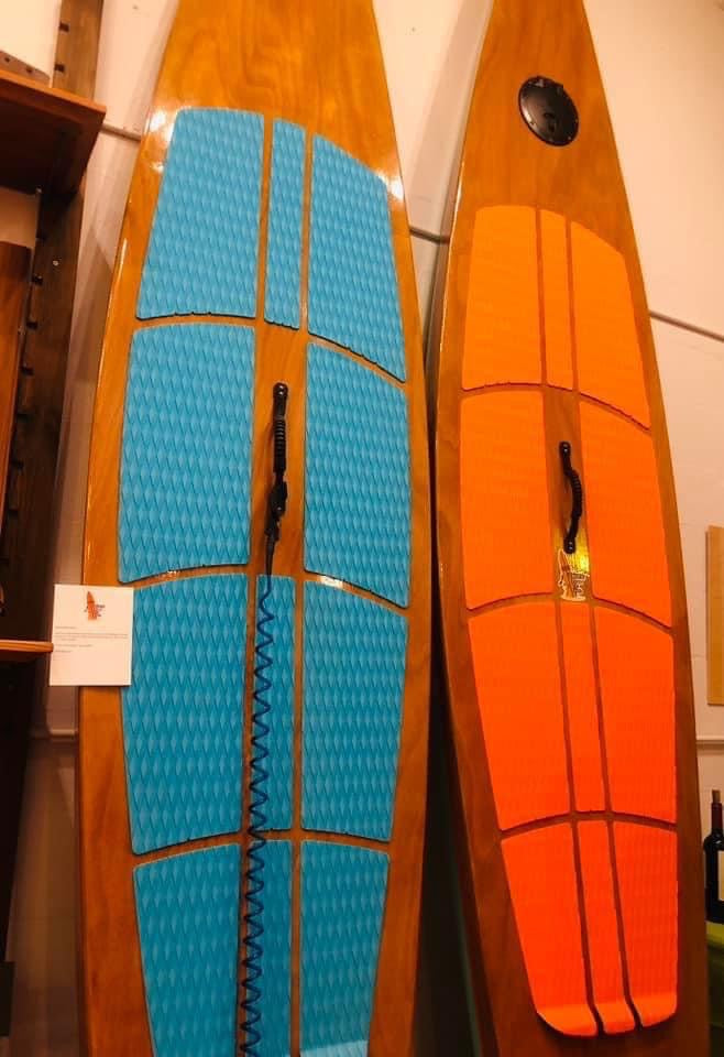 gorgeous wood paddleboards, one with turquoise colored rubber padding and the other with orange colored rubber padding